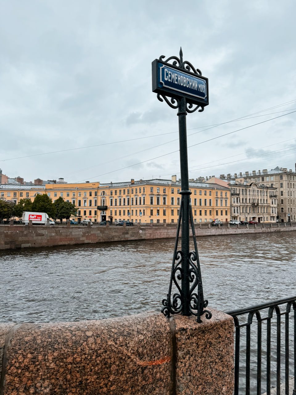 Кованый указатель «Семёновскій мостъ» у реки Фонтанки на фоне жёлтого дома, Петербург